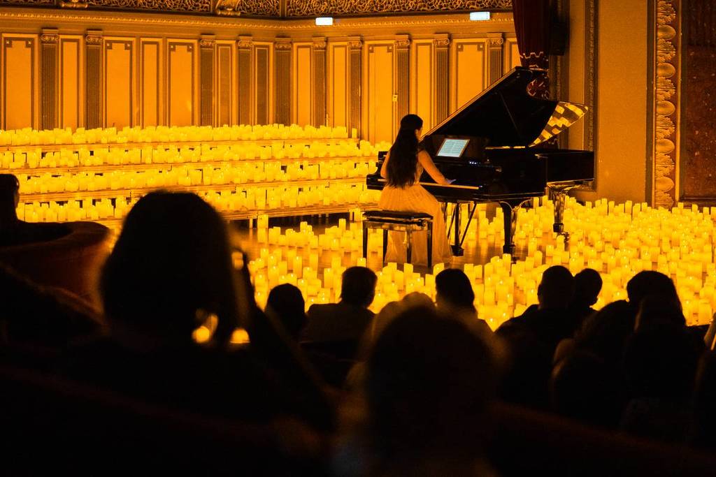 The silhouettes of audience members watching a pianist perform on stage surrounded by a sea of candles