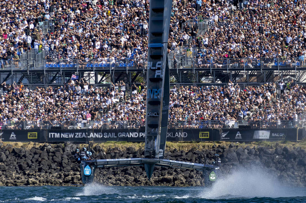 A close up shot of a F50 catamaran skimming the top of the water in front of a packed stadium.