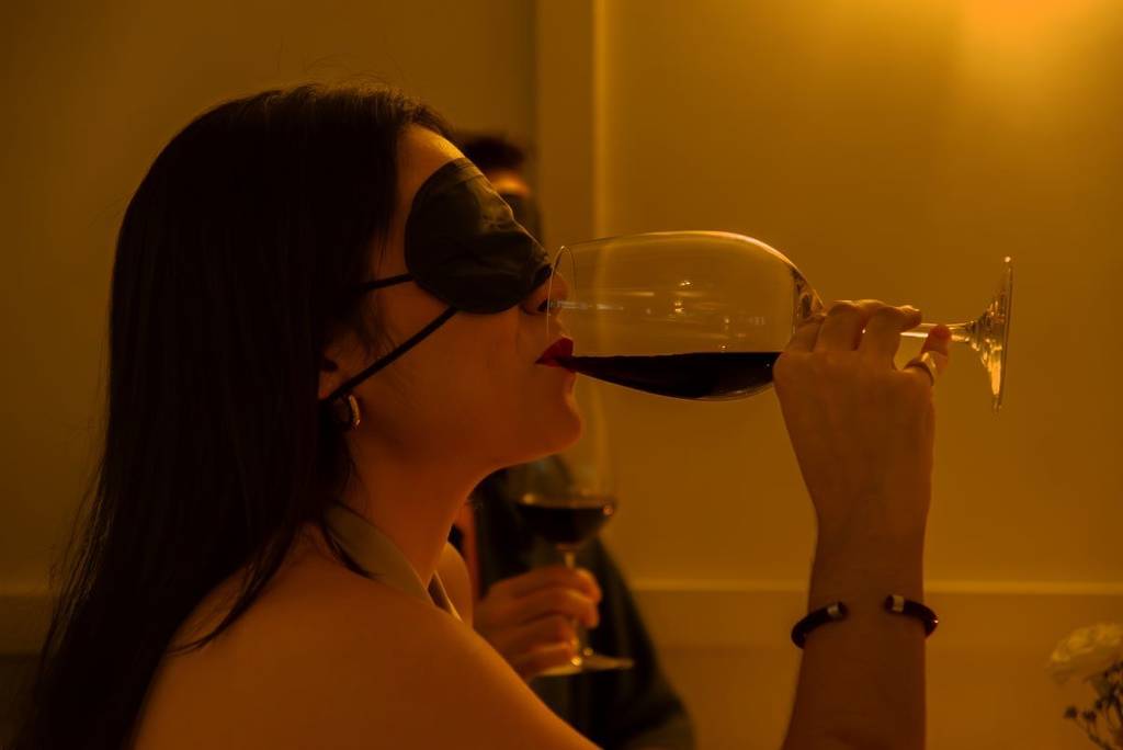 A woman sipping a glass of wine, blindfolded, at Dining in the Dark.