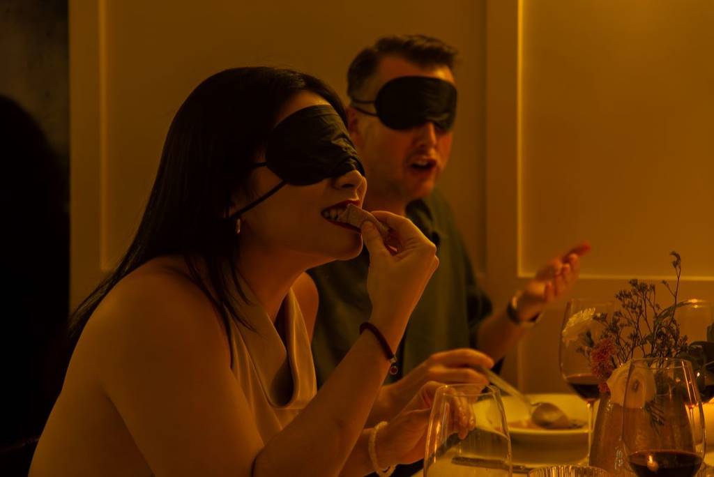 A woman trying food, blindfolded, at the Dining in the Dark experience.