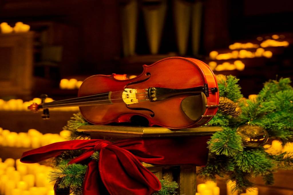 Viool samen met kerstversiering op de voorgrond, verschillende brandende kaarsen op de achtergrond tijdens een kerstconcert bij kaarslicht