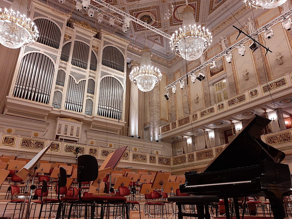 Konzertsaal im Konzerthaus Berlin, Bühne mit Flügel und aufgereihten Stühlen fürs Orchester, prunkvolle Kronleuchter an der Decke