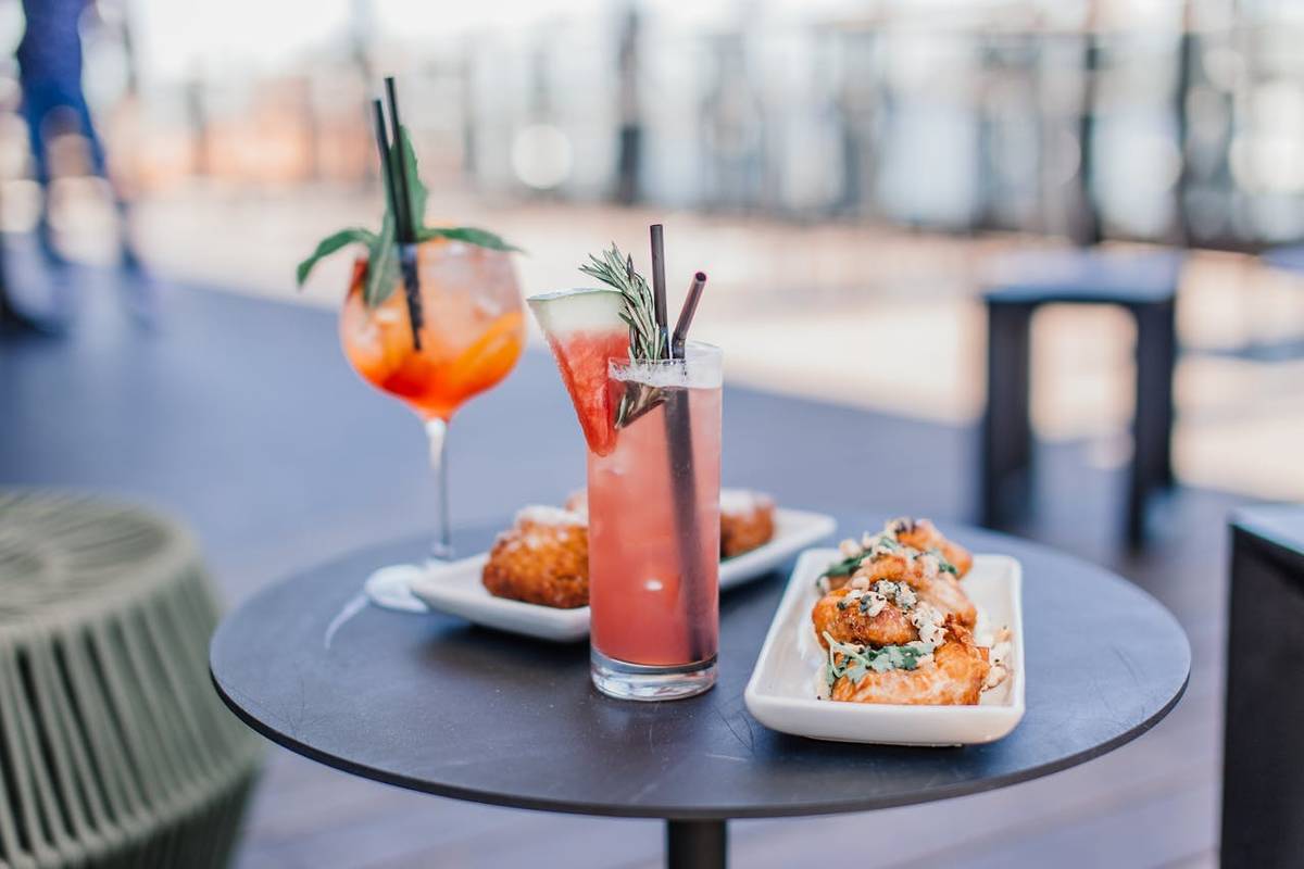 Zwei Cocktails und zwei kleine Teller mit Essen stehen in einer Open Air Bar auf einem runden Tisch