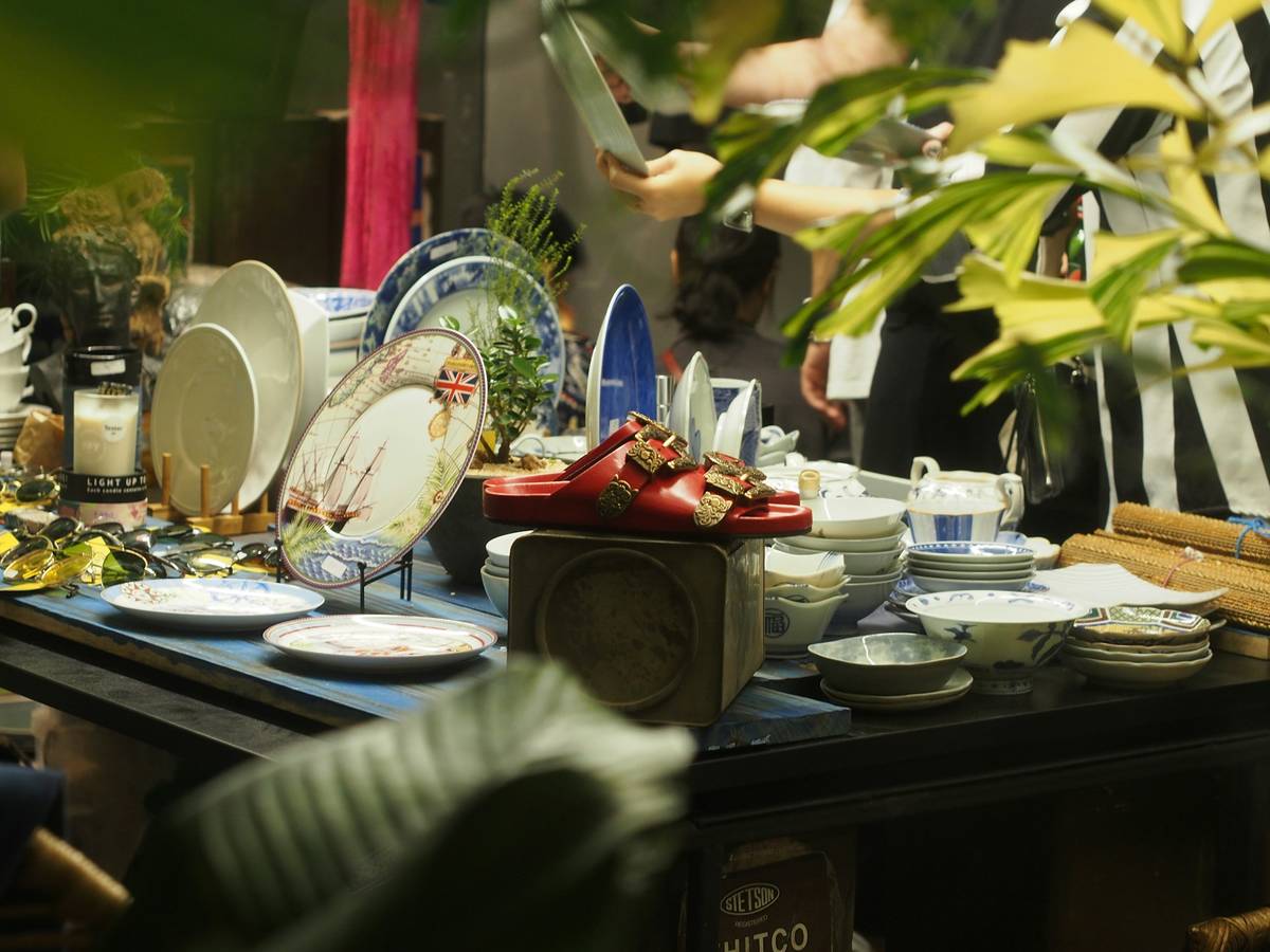 Vintage Flohmarktstand mit Tellern, Schüsseln und roten Schuhen, Pflanze im Vordergrund