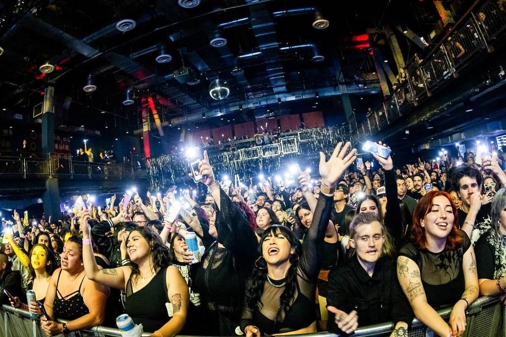 People dance and sing on the dance floor at Emo Night Brooklyn while holding up their cell phone lights.