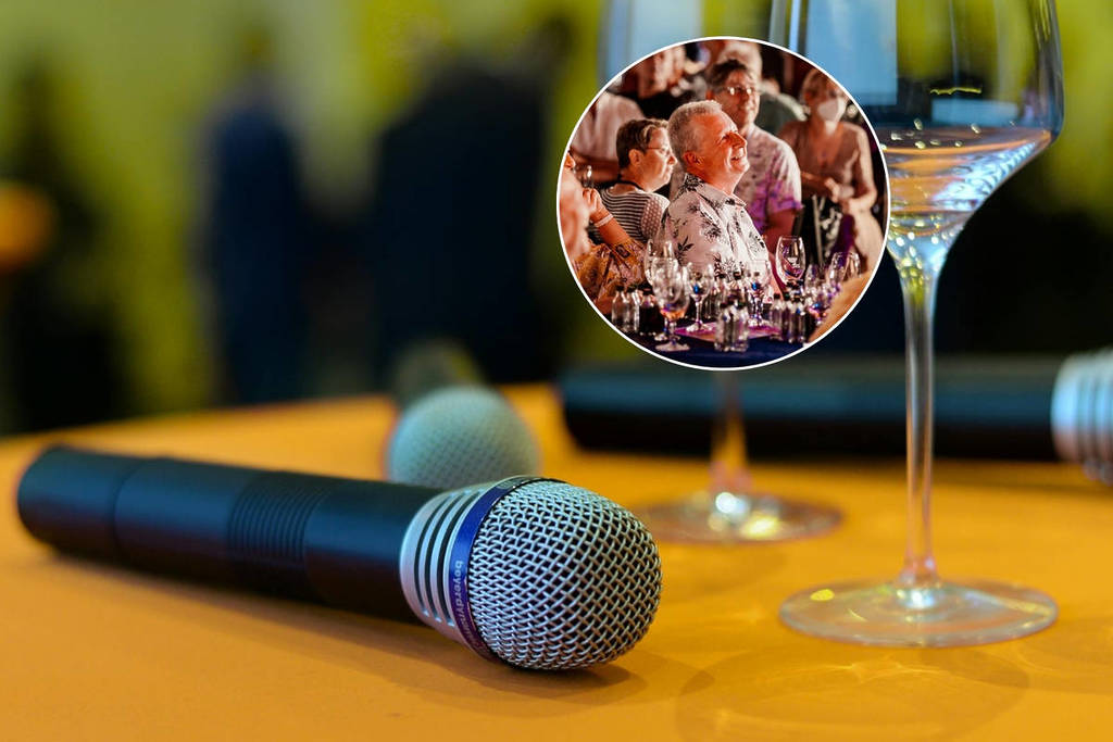Microfoons liggen naast lege wijnglazen op een tafel | lachend publiek bij 