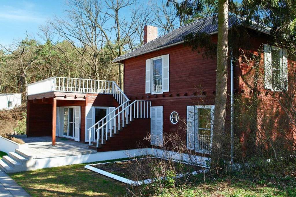 Vista esterna della casa estiva di Albert Einstein. La semplice costruzione in legno rosso scuro affascina con le sue persiane bianche e una scala esterna bianca che conduce a un’ampia terrazza.