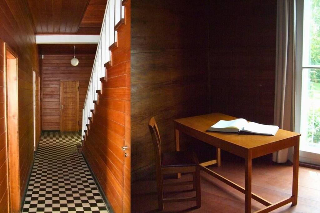 Immagine divisa in due che mostra gli interni: a sinistra il corridoio rivestito in legno della casa, a destra un semplice studio con una semplice scrivania di legno e un libro aperto davanti a una grande finestra.
