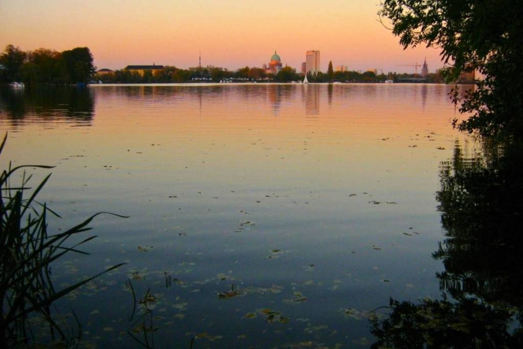 Vista sulle acque tranquille del lago di Templin durante un dolce tramonto. Sullo sfondo, all’orizzonte, si staglia la sagoma di Potsdam.