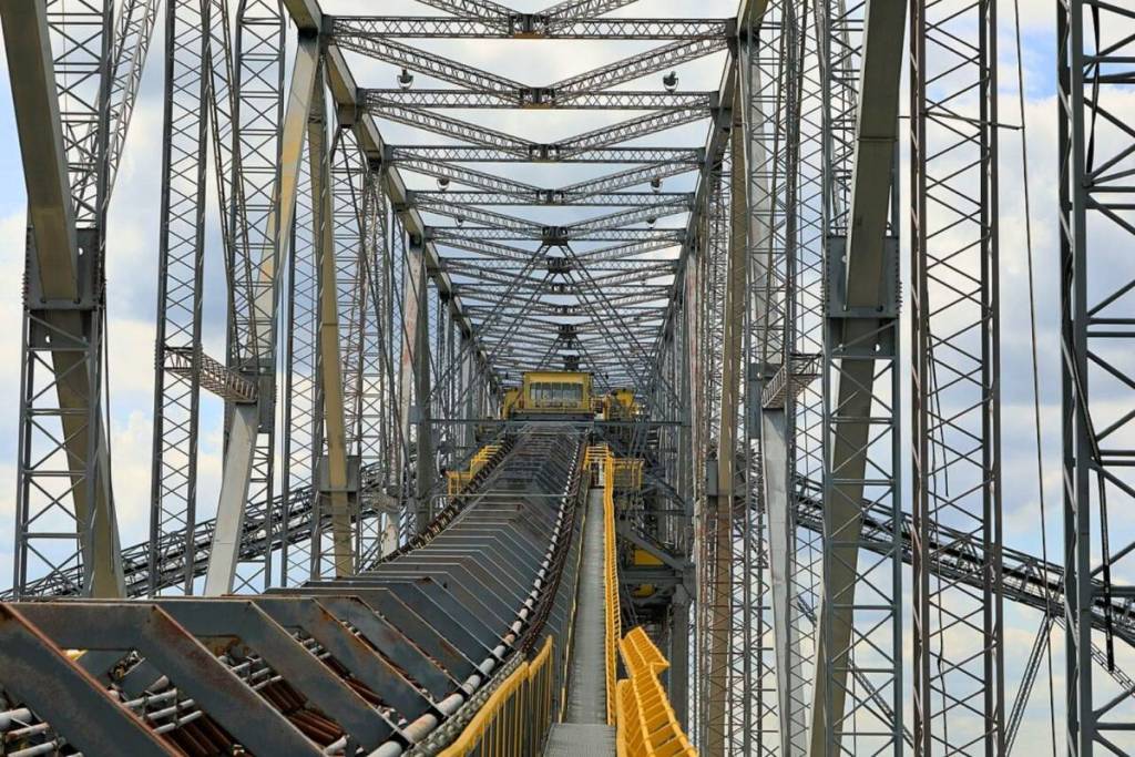 Symmetrischer Blick aus dem Inneren der massiven Stahlkonstruktion der F60 Abraumförderbrücke in Lichterfeld, Lausitz. Man sieht Gitterwerk und Förderbänder unter einem abendlichen Himmel.