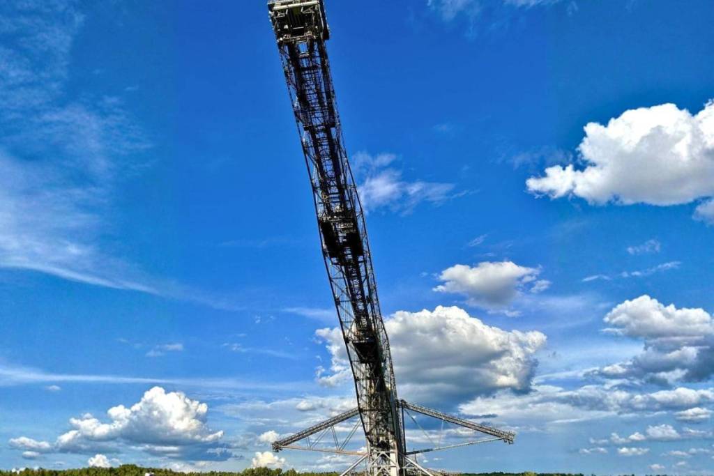 Una spettacolare prospettiva dal basso che guarda verso l’alto lungo un imponente pilone del ponte trasportatore di sterili F60, davanti a un cielo blu splendente con nuvole bianche.