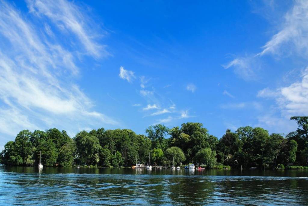 L’île de Valentinswerder, verdoyante et densément boisée, sur le lac de Tegel à Berlin, avec de petits voiliers au bord de l’eau sous un ciel d’un bleu éclatant.
