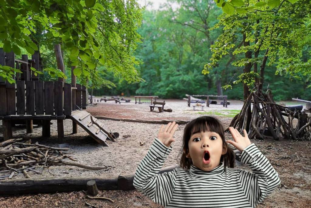 Überraschtes Mädchen freut sich über den großen Holzspielplatz im Plänterwald Berlin, im Hintergrund stehen hölzerne Spielgeräte und aufgestellte Äste zum Spielen.