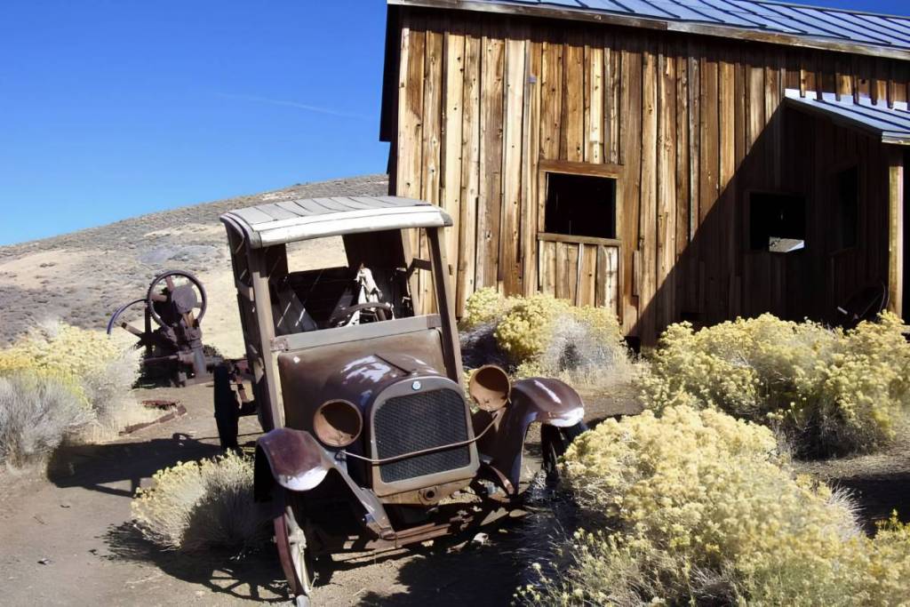 Rostiger Oldtimer-Lastwagen vor einer historischen Holzhütte in der Geisterstadt Berlin, Nevada, unter blauem Himmel.