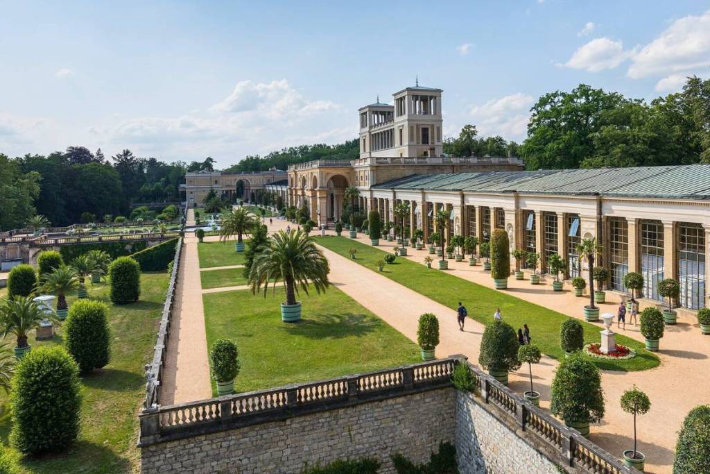 Weids uitzicht op de historische plantenhuizen en terrassen van het 300 meter lange Orangerie-paleis in Potsdam, met palmbomen en sinaasappelbomen.