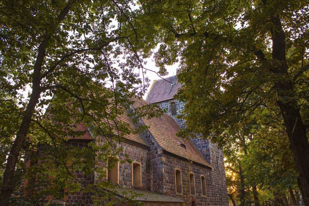 L’église médiévale en pierres des champs de Marienfelde, à Berlin, entourée d’arbres verdoyants sous les rayons du soleil.