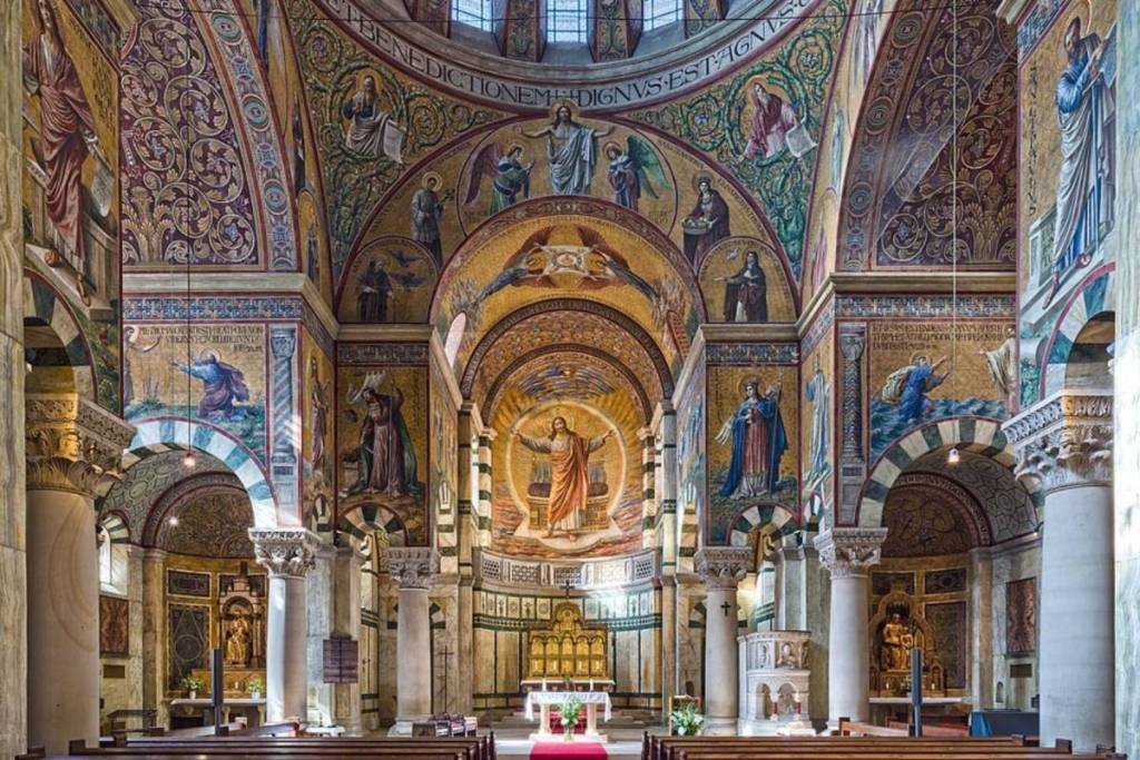 El magnífico interior de la iglesia del Sagrado Corazón de Jesús en Berlín, con columnas macizas, pinturas murales bizantinas y un presbiterio dorado.