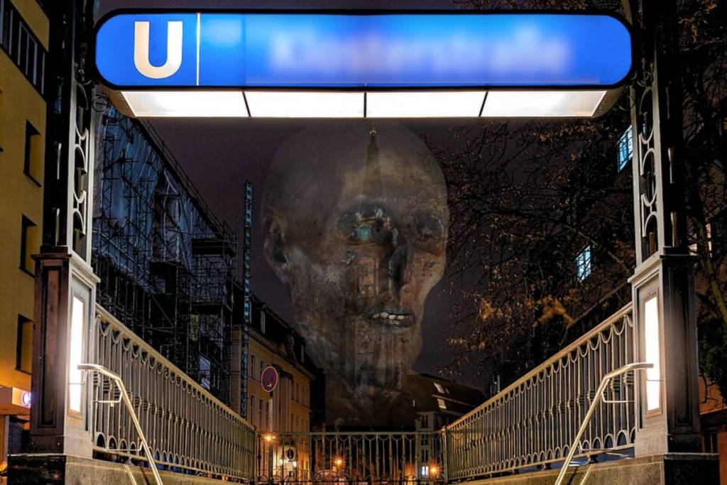 Nachtelijke visualisatie van de legende van de ‘Rote Else’: een gigantisch, spookachtig mummiehoofd zweeft boven de verlichte ingang van het metrostation Klosterstraße in Berlijn-Mitte, waar in 1986 een mummie werd gevonden.