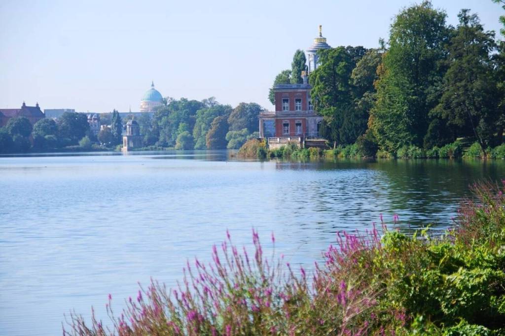 A sweeping view across the lake in the UNESCO World Heritage Site Neuer Garten, looking toward the red marble palace and the small Gothic Library in the background.