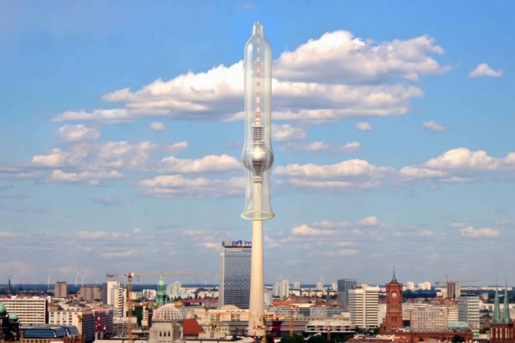 Alt-Text: Ein riesiges durchsichtiges Kondom über dem Berliner Fernsehturm vor blauem Himmel als Symbol für die Erfindung des Gummi-Kondoms in Berlin.