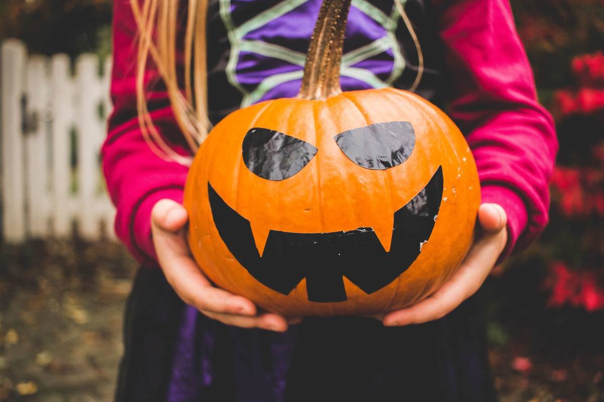 A child holding a pumpkin with a face painted on it