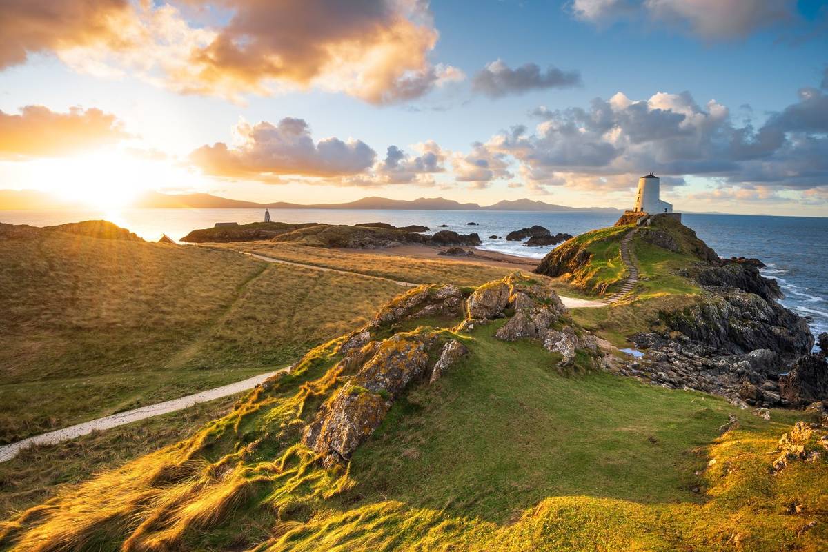 Golden sunrise at Twr Mawr Lighthouse on Ynys Llanddwyn Island on The Coast of Anglesey, North Wales with Snowdonia mountains in background.