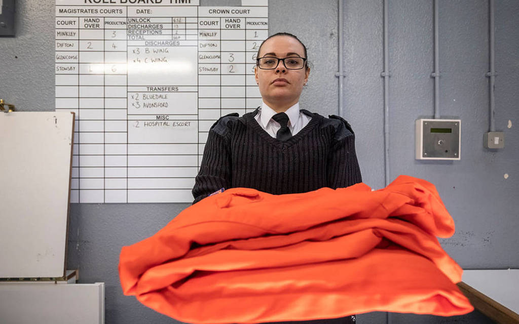 a prison guard holding orange jumpsuits at Shrewsbury Prison