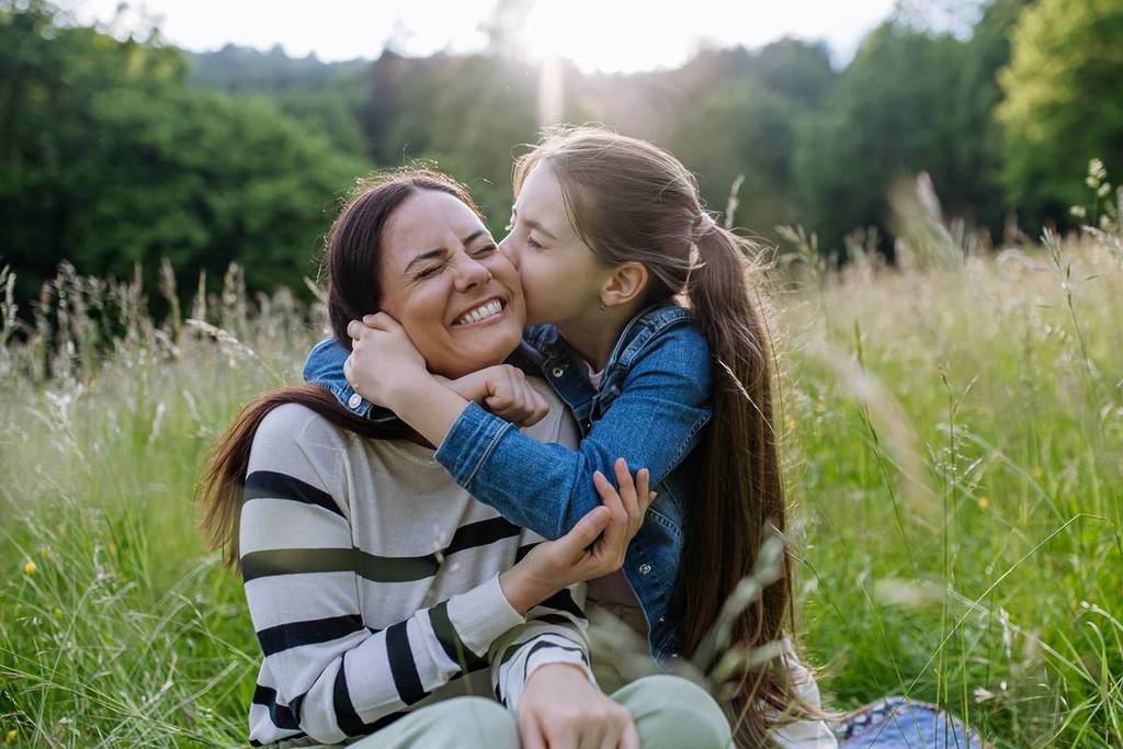 A mom and daughter in a meadow hugging