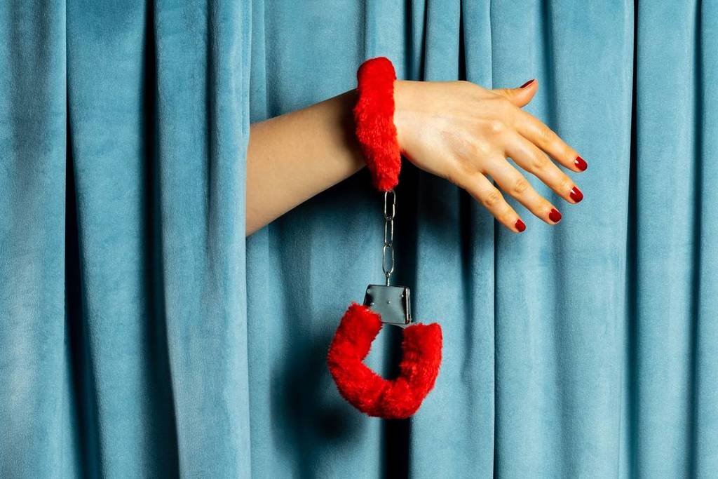 Woman hand in red fluffy handcuffs on the background of a blue velvet curtain