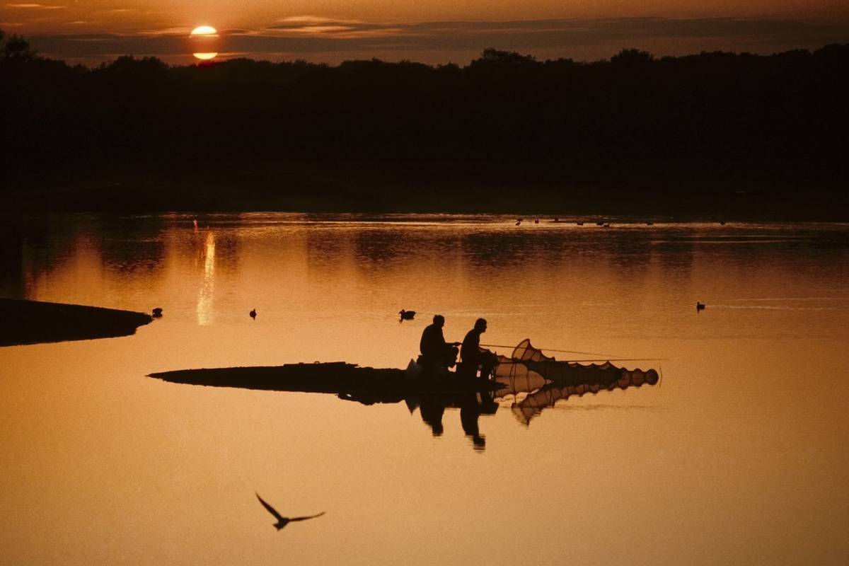 fishermen fishing on lake with sunset behind earlswood lakes warwickshire midlands england uk