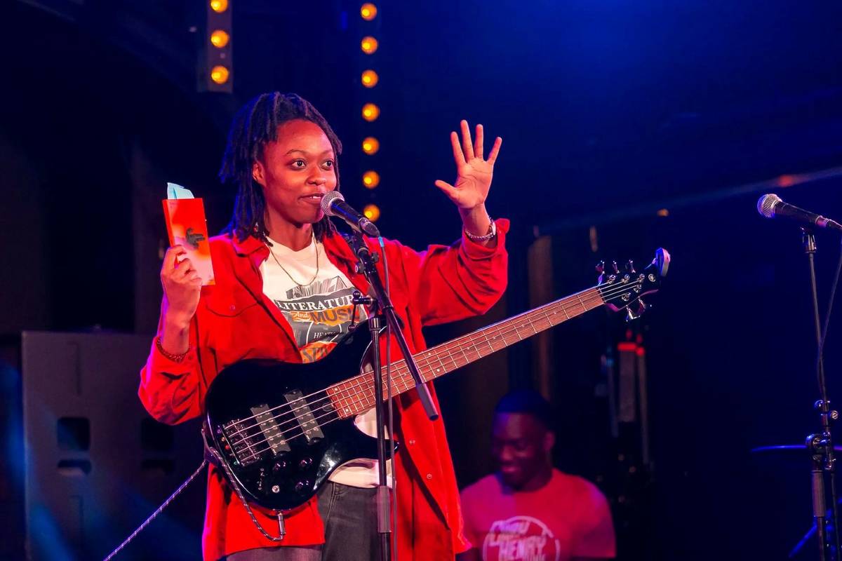 A bassist at a microphone wearing a The Heath Bookshop Literature And Music Festival T-shirt