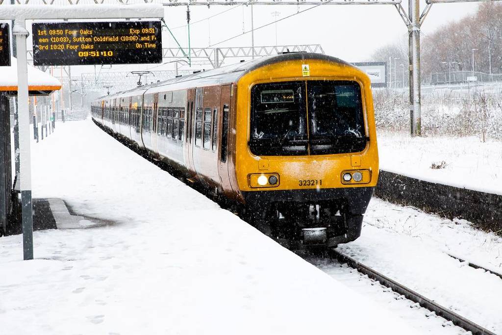 DUDDESTON, BIRMINGHAM, UK - MARCH 9, 2023. A West Midlands Trains passenger service at a snow covered station platform with heavy snowfall causing travel disruption