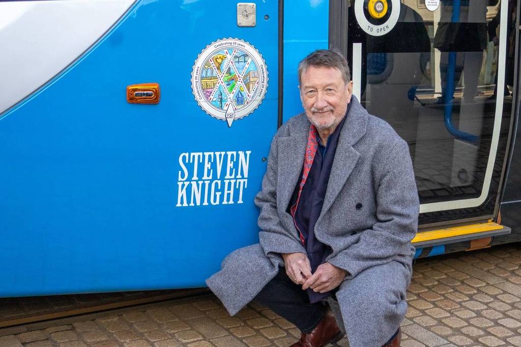 Steven Knight kneeling in front of a West Midlands Metro tram