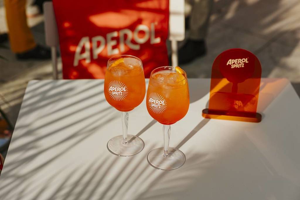 two aperol spritz on a white table with aperol sign in the background