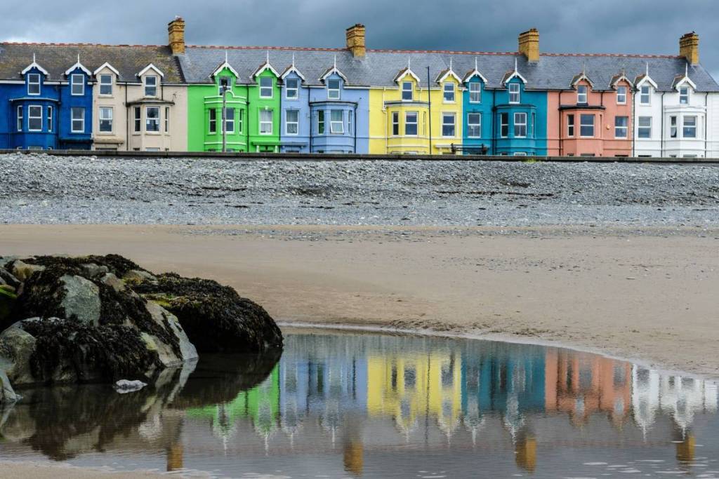 Borth, Ceredigion, Wales - June 12 2019: Multi-coloured houses overlooking the beach at Borth with a foreground of weed covered rock and reflections of the houses in a pool of wet sand.