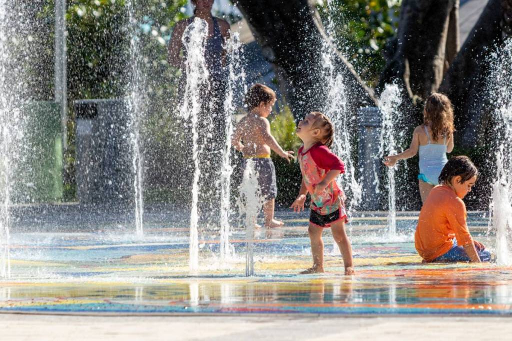 Children in bathing suit playing in the splash pad water fountain in the summer holidays mothers and parental guardians nearby watching