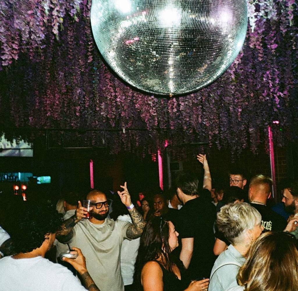 a group of people dance in a club under a giant disco ball