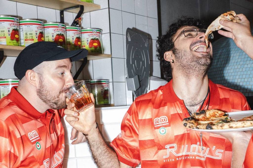 Two men eating pizza and drinking Negronis in Rudy's football shirts