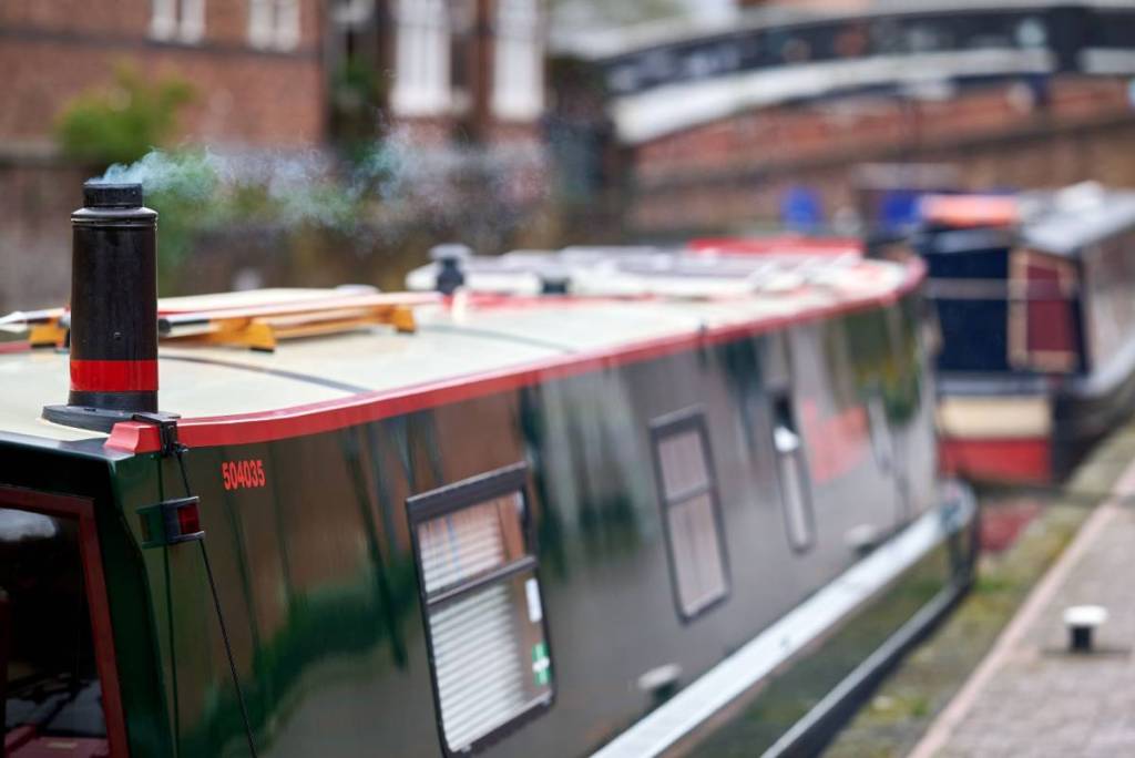 Smoke rising from the chimney of a narrowboat moored on the canal at Gas Street Basin, Birmingham, West Midlands, England, UK.