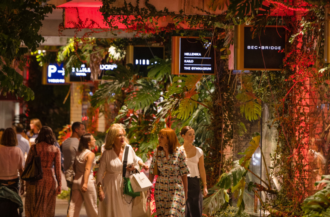 a photo of people walking on a street at night next to some boutique shops