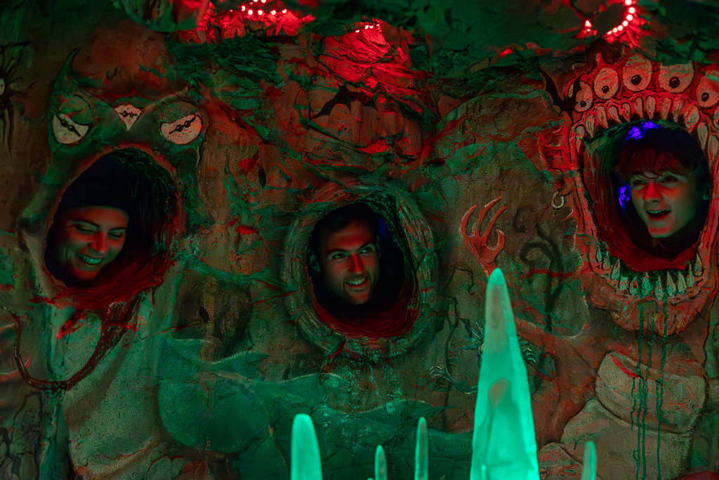 Three people stick their heads through peepholes in a tree to see the glowing decorations inside at LUMA Enchanted.