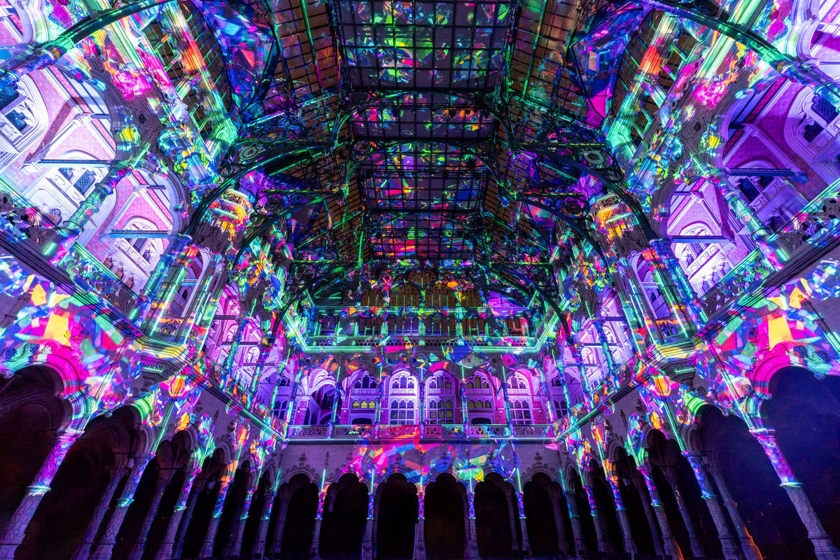 The ceiling and walls of an old building with lots of windows and arches are covered in pink, green and blue lights, projected as part of the Enlightenment show.