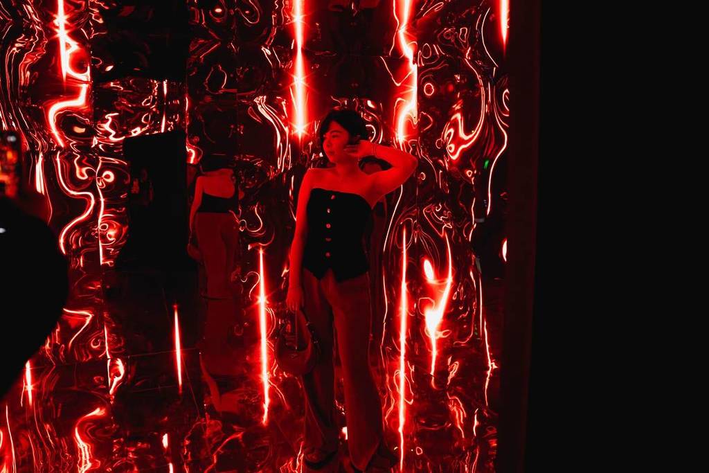 A young woman stands in a room lit up with red lights at Dopamine Land.