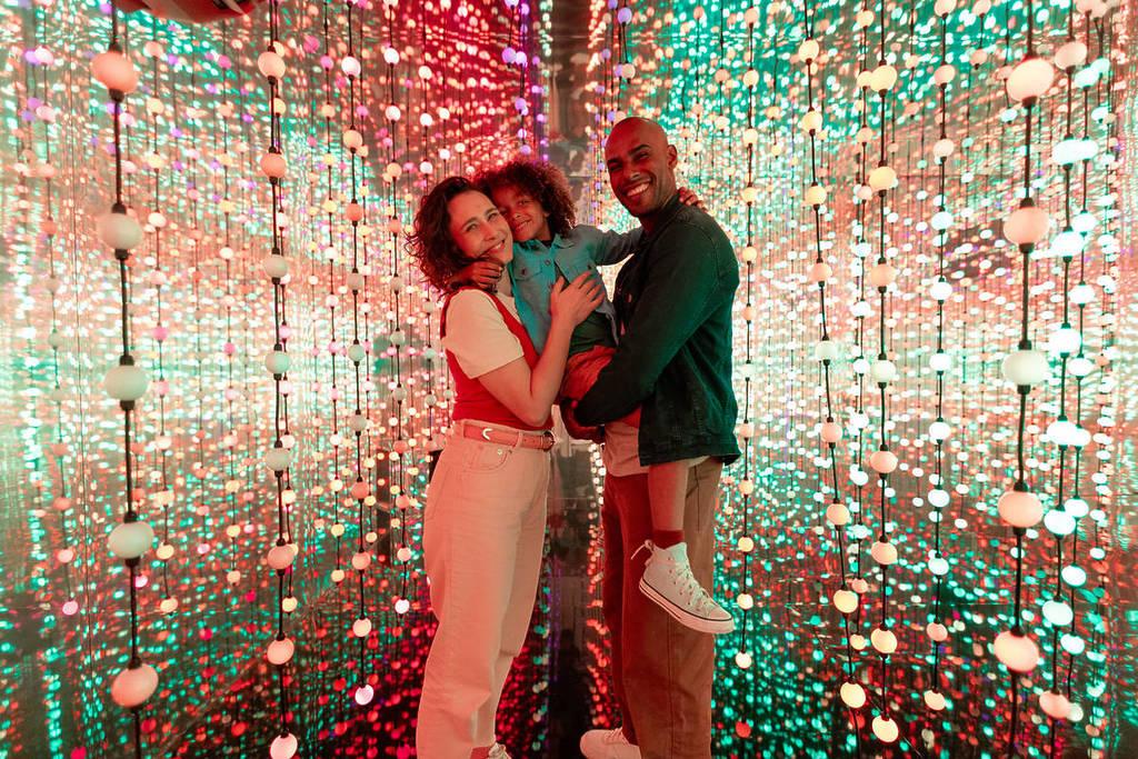 Two parents hold up their child to pose for a photo in the infinity room at Dopamine Land.