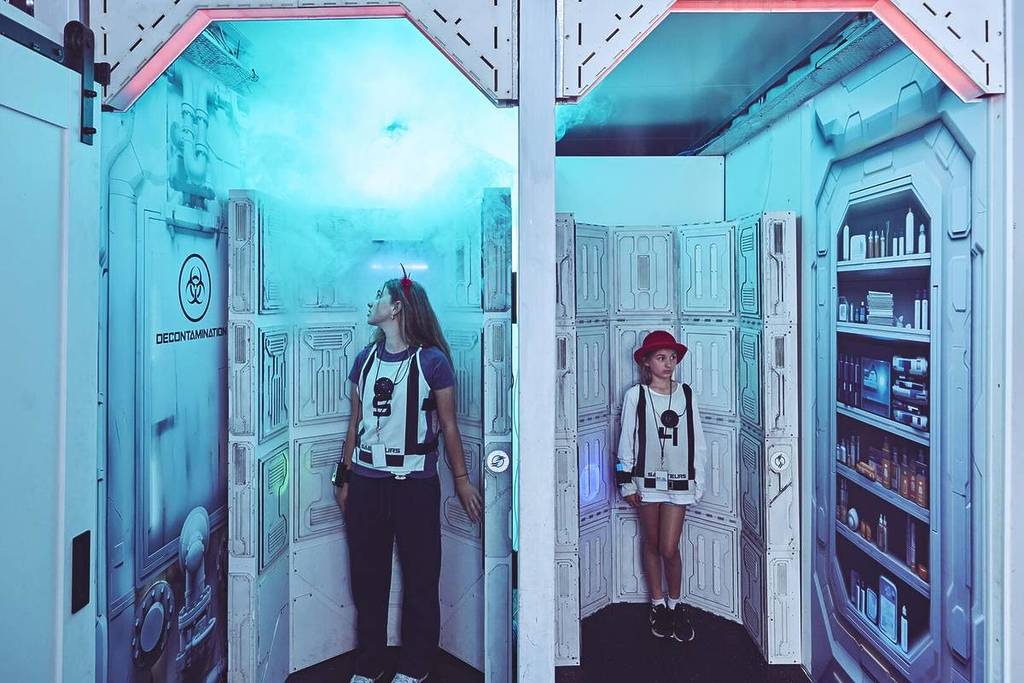 A boy and girl stand in separate decontamination pods at Saboteurs.
