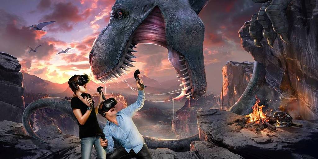 A man and woman in VR headsets at Virtual Room duck away from the mouth of a giant T-rex.