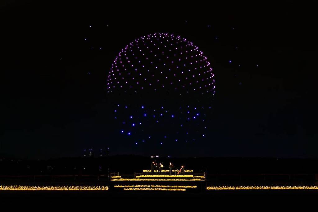 An image of a dome created by drones is pictured in the sky above a candlelit orchestra at DroneArt Show.