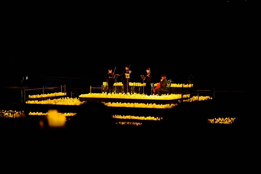 An orchestra performs on a stage surrounded by candles.
