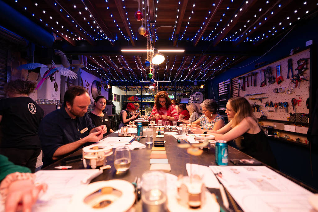 A group of people building sculptures at a shared workbench at Sculptures & Sips.