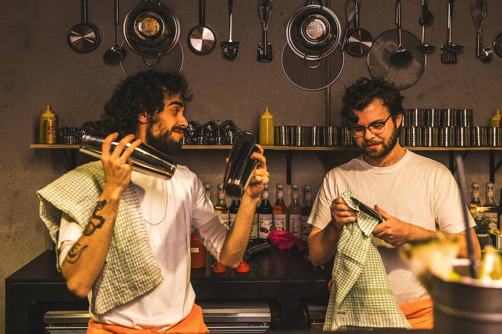 Two men in orange jumpsuits mix cocktails behind a bar at Alcotraz.
